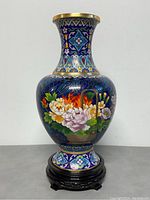 Front view of vintage Chinese royal blue cloisonne vase featuring vibrant floral motifs and wooden display stand base.