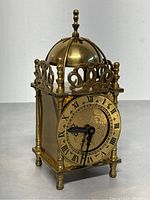 Front angled view showing brass dome bell, ornate top details, and clock face with Roman numerals and decorative engravings.