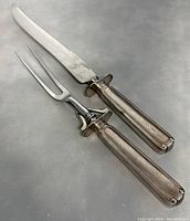 Photo of the two-piece carving set: a knife and fork with sterling silver handles on a grey surface.
