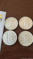 Four silver dollar coins laid out showing reverse totem pole design
