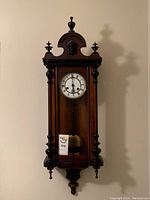 Full front view of the antique Junghans wooden wall clock with pendulum and ornate top detailing.