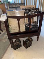 Full view of the dark wood Canterbury rack holding six large vintage books and two metal bookends beneath.