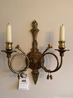 Pair of matching brass candle sconces mounted on wall, each holding two cream-colored candles.