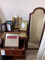 Photo showing assortment of picture frames on a wooden table and a full-length mirror standing on the floor leaning against the wall.