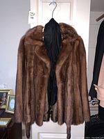 Front view of brown mink fur coat hanging on hanger showing full collar and plush texture.