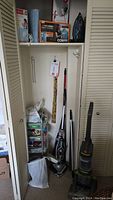 Full view of storage closet holding multiple cleaning and home care appliances, irons, heating pads, utility cart with supplies.