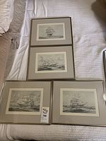 All four framed Ken Foster art prints laid out on a bed, showing the black and white sailing ship images with mats and frames.