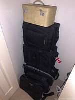 Photo showing stacked luggage including the beige textured hard case on top and black backpacks and carry-ons underneath.