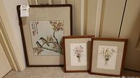 All three framed art pieces leaning against a door: one larger bird illustration and two smaller floral prints