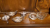 Overall view of all sterling silver serveware pieces with ladles and two cut glass bowls on wooden surface