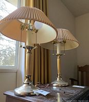 Pair of vintage brass table lamps with pleated beige fabric shades, showing lamp bases, pull chain switches, and lampshades.