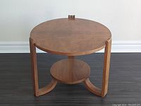 View of the round burl walnut top, lower circular shelf, and curved leg supports of the Art Deco side table.