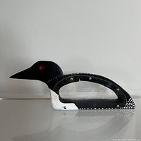 Side view of wooden loon coin bank showing black and white paint, red eye, and clear acrylic panel secured by screws.