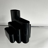 Front angled view of glossy black plastic desk organizer with six connected compartments of different sizes and shapes.