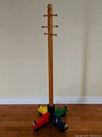 Full view of the wooden coat rack standing against a wall, showing the tall vertical pole with several hooks at the top and the colorful train base on the floor.