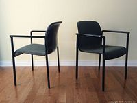 Pair of vintage Herman Miller lounge chairs front and side view, showing dark upholstered seats and tubular black steel frames.