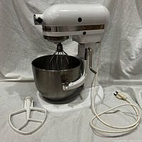 Front view of white KitchenAid mixer seated in stainless steel bowl with flat beater on tabletop