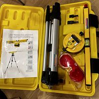 Laser level kit items including tripod, laser level base, safety glasses, and manual inside yellow carrying case.