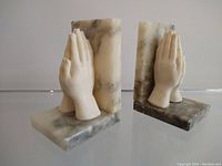 Pair of carved praying hands marble bookends, side and angled view showing realistic hand sculpture and marble base with veining.
