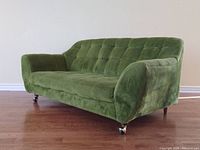 Front three-quarter view showing tufted back, sloped arms, caster wheels