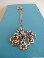 Full view of the necklace laid flat, showing the pendant and chain on a blue background.