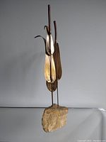 Full front view of the bullrush sculpture showing brass and copper leaves and stalks rising from a natural stone base.