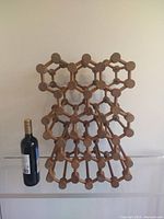 Front angle view showing the full height and molecular pattern of the wooden wine rack with a bottle placed beside it for scale.