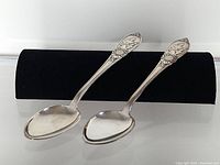 Pair of silver serving spoons placed side by side on black velvet, showing the overall shape and size.