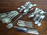 Photo showing various forks, spoons, and knives laid out on wooden surface with visible tarnish.