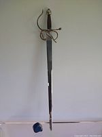 Full view of the Spanish ceremonial rapier hanging vertically, showing polished blade, copper wrapped handle, and silver plated guard.