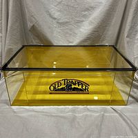 Front view of the Old Trapper display storage case showing yellow-tinted acrylic and printed logo on front panel.