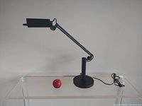 Full view of black Atelio vintage desk lamp on clear surface with visible power cord, showing adjustable arm and rectangular head.