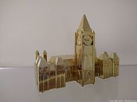 Full front view of vintage brass-colored Canadian Parliament building piggy bank showing central clock tower and flanking structures.