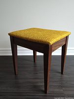 Front side view of the wooden stool with yellow woven fabric seat, showing the square shape and straight, tapered legs.