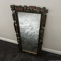 Full view of the large Brutalist style rectangular wall mirror with textured resin frame leaning against a wall on carpet.