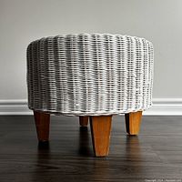 Side view of the vintage white wicker ottoman showcasing the woven texture and wooden legs.