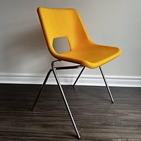 Front angle view of yellow Ikea Järvi chair with chrome legs on dark floor