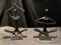 Two black metal yoga figurines side by side on a textured surface with a black backdrop, showing both meditation and stretching poses.