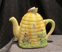 Front side view of beehive ceramic teapot with bee figurine lid and floral design