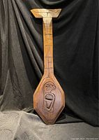 Full view of the entire carved wooden paddle against black fabric, showing shape and size