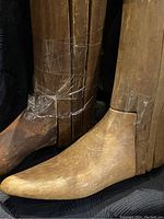Close-up photo showing the wooden toe and lower leg areas of two antique boot trees with tape and repair bindings.