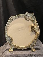 Front view showing full round brass frame with female figure and floral decorations.