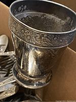 Close-up of a silver goblet featuring floral and bird engravings with visible tarnish.