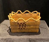 Front and side angle view of a rectangular Coast Salish basket with zigzag rim and checkered accent.