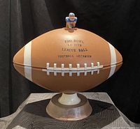 Front view of the football-shaped decanter with text on the front showing 'Pro Bowl 1773 League Ball Football Decanter' mounted on a wooden base.
