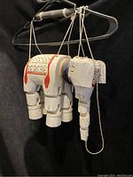 Side view of white wooden Thai elephant marionette hanging by strings from a black hanger