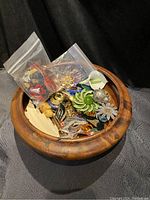 Clear view of exotic wooden bowl filled with assorted brooches and two small plastic bags containing earrings.