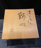 Closed wooden box with Asian characters on the lid, possibly the original container or presentation box for the plate
