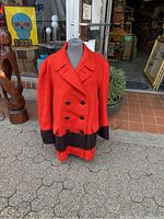 Front angle view of the red and black thick wool coat on a mannequin outside a shop.