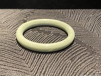 Close-up photo of a pale green jade bangle bracelet lying on a textured black fabric background, showing smooth and polished surface with natural color variation.